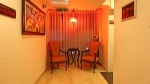 A room with two upholstered chairs, a small table, a painting on the wall, and an exit sign. - Divinity By Audra Hotels (Mathura)