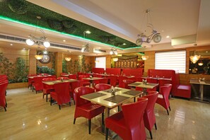 A restaurant with red chairs and tables, green ceiling accents, and decorative wall elements.