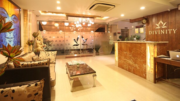 A reception area with a marble reception desk, a sofa with patterned cushions, a coffee table, and a wall with a 'DIVINITY' logo. - Divinity By Audra Hotels (Mathura)