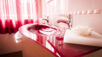 A modern bathroom with a red sink, chrome faucets, and a white rose on a napkin.