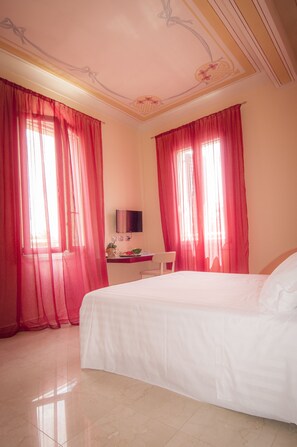 Una habitación de hotel con una cama grande, un escritorio con una silla, un televisor y cortinas traslúcidas rojas.