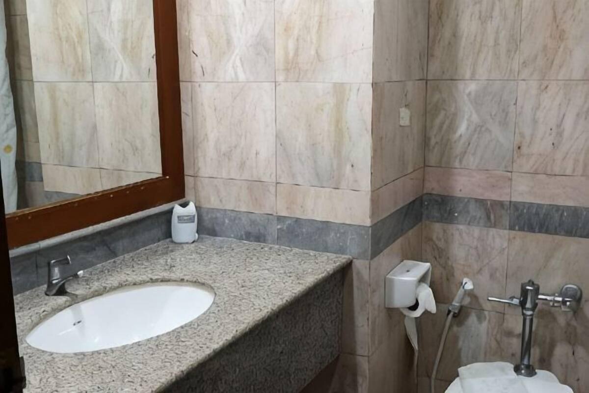 A bathroom with a granite countertop, a sink, a mirror, a towel dispenser, and a toilet with a bidet attachment.
