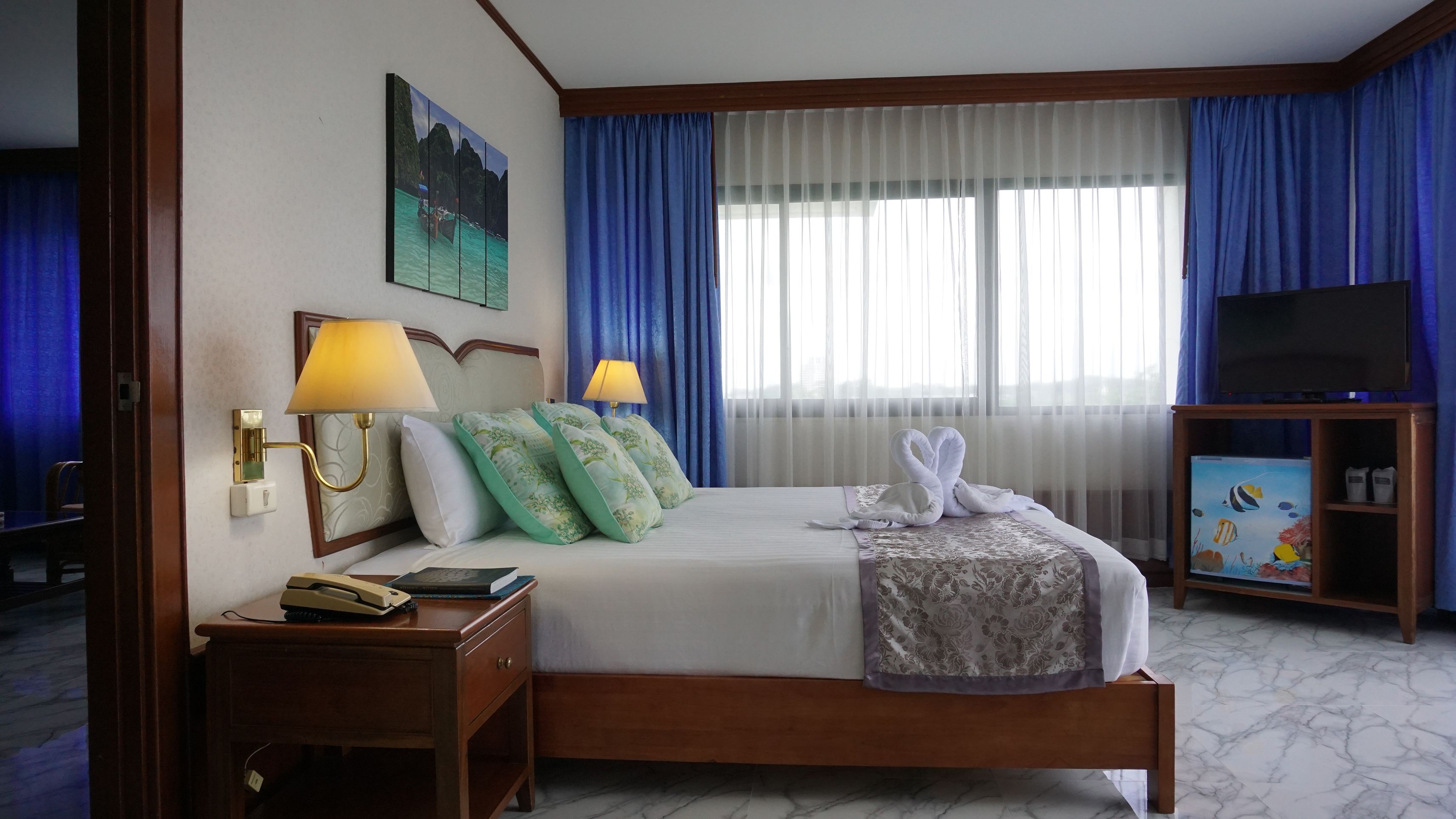 A hotel room with a bed, two bedside lamps, a painting, a television, and a small cabinet.