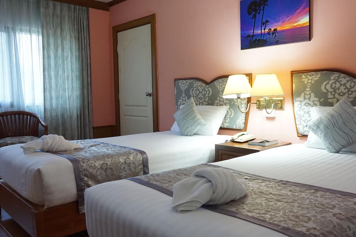 A hotel room with two beds, a nightstand with a lamp, a telephone, and a painting of a sunset on the wall.