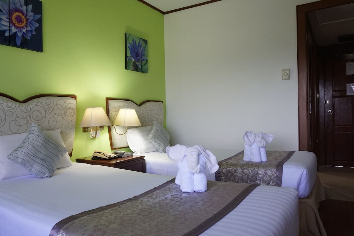 A hotel room with two beds, a nightstand, lamps, and artwork on the walls.