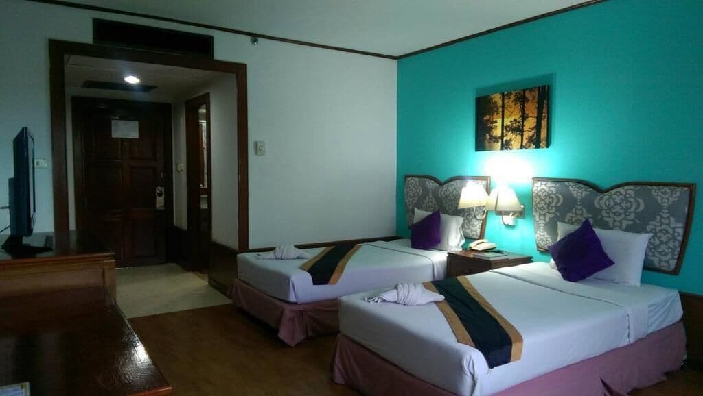 A hotel room with two beds, a desk, a TV, and a door leading to another room.