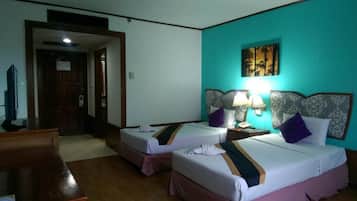 A hotel room with two beds, a desk, a TV, and a door leading to another room.