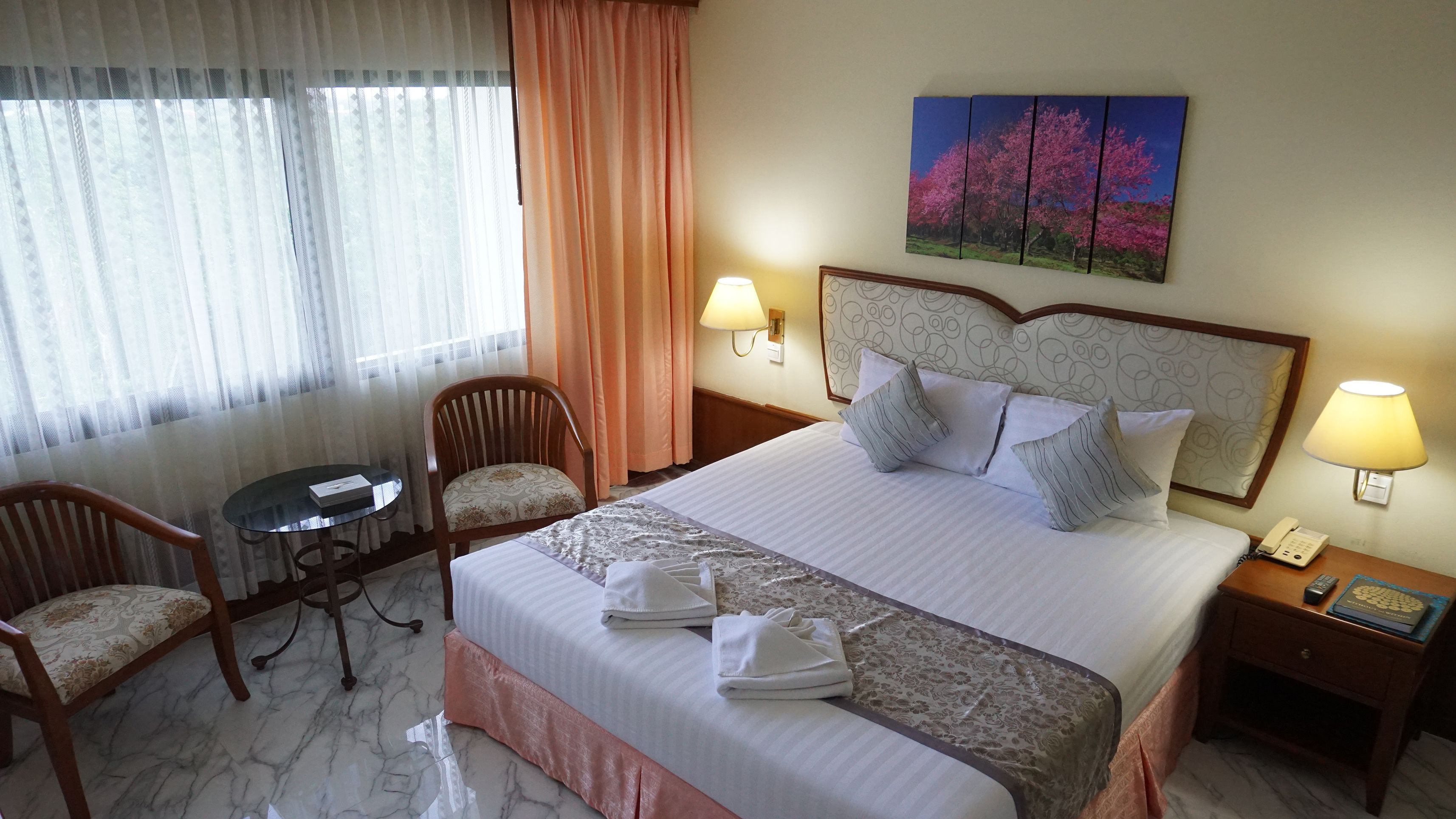 A hotel room with a large bed, two bedside tables, a desk, and two chairs.