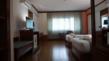 A hotel room with a bed, a desk with a computer, a chair, and a window with curtains.