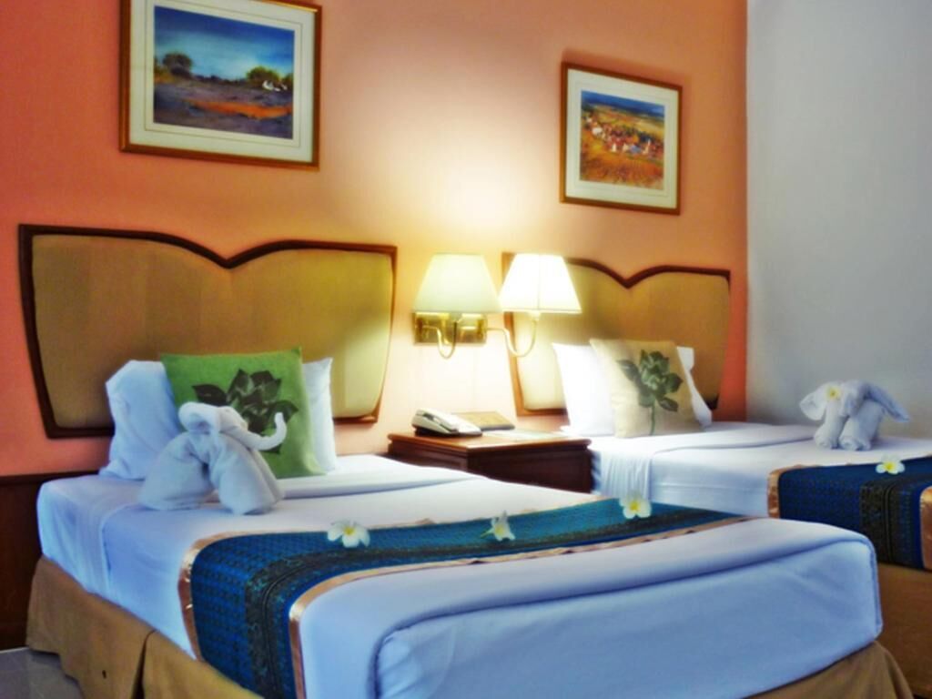 Habitación de hotel con dos camas, cada una con una almohada y una toalla. Hay dos lámparas de pared y dos cuadros enmarcados.