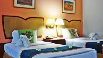 Habitación de hotel con dos camas, cada una con una almohada y una toalla. Hay dos lámparas de pared y dos cuadros enmarcados.