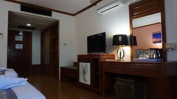 Habitación de hotel con escritorio de madera, televisor de pantalla plana, lámpara, cafetera y un cuadro enmarcado.