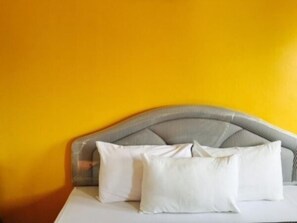 Una cama con cabecera a rayas frente a una pared amarilla.