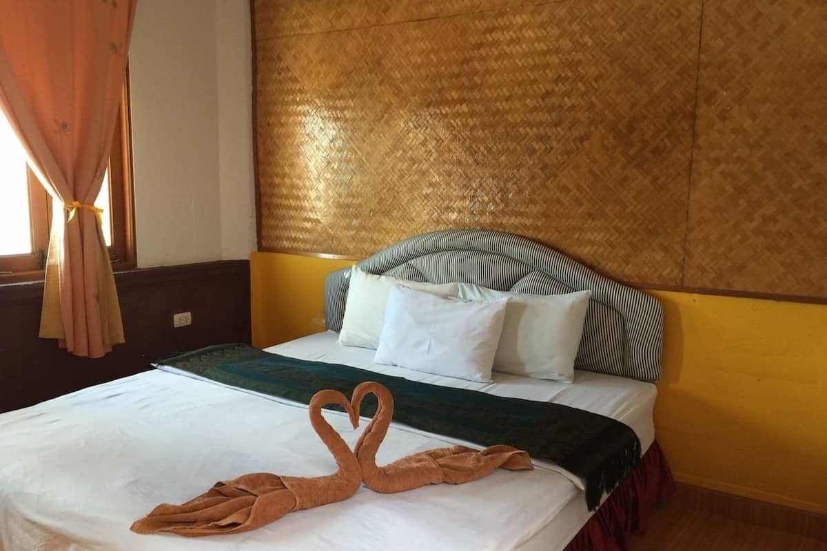 Una habitación de hotel con cama, cabecera a rayas y una toalla dispuesta en forma de corazón.