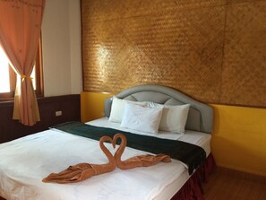 Una habitación de hotel con cama, cabecera a rayas y una toalla dispuesta en forma de corazón.