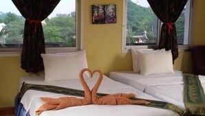 A hotel room with two beds, a view of greenery outside, and a painting on the wall.