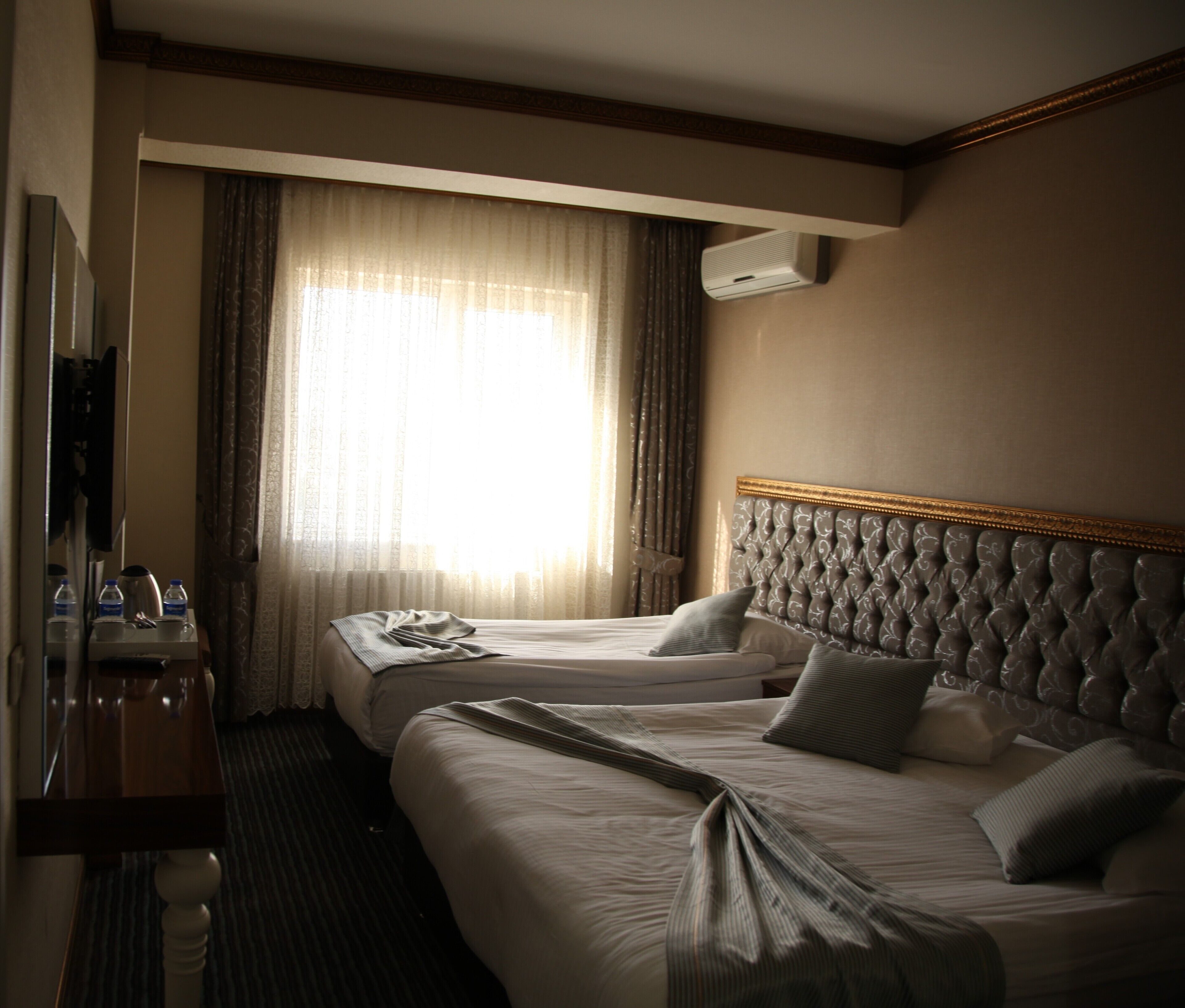 A hotel room with two beds, a desk, a mirror, and an air conditioning unit.