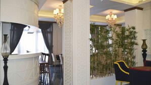 Un hall de hotel con mostrador de recepción, sillas, una planta de bambú y candelabros.