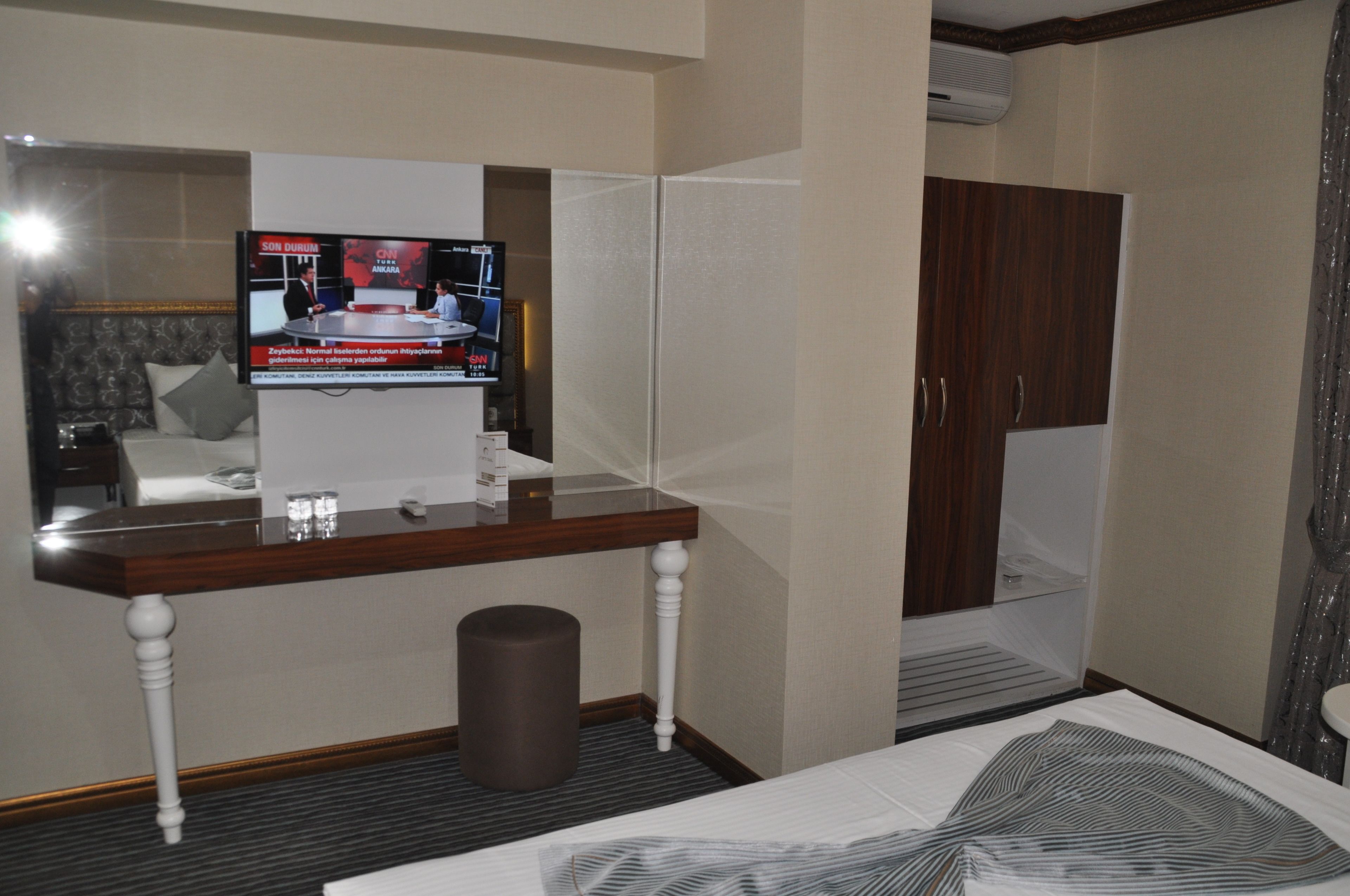 Une chambre d’hôtel avec un téléviseur posé sur un meuble en bois, un lit, une armoire et une petite poubelle.