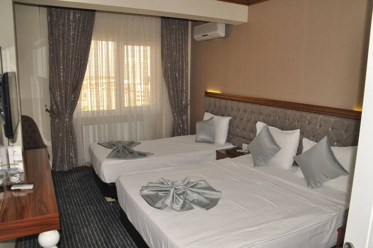 A hotel room with two beds, a TV, a desk, and a window with curtains.