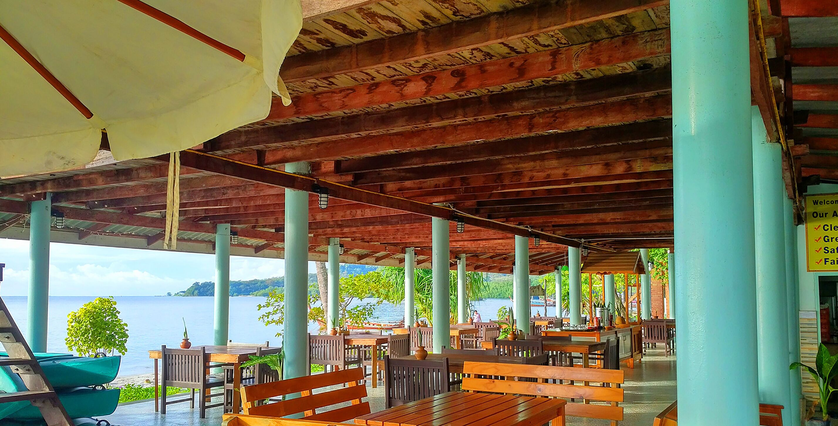 A covered outdoor seating area with wooden benches and tables, overlooking a body of water.