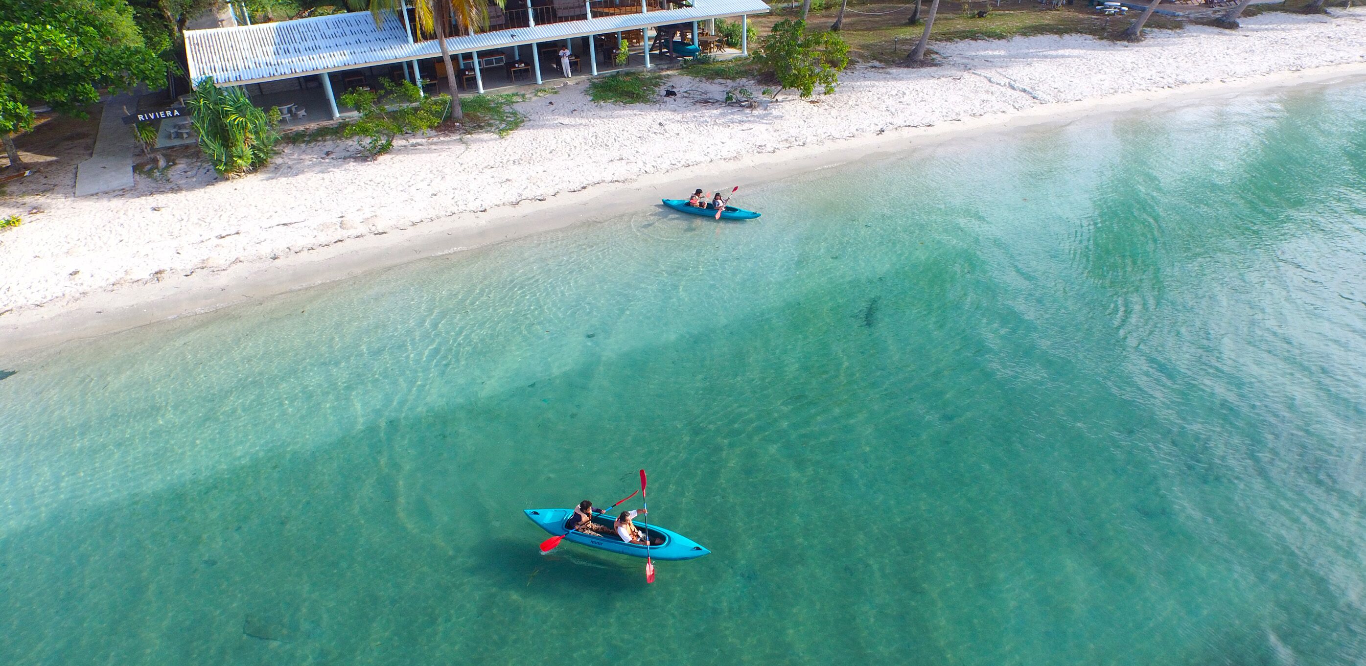 A beach with clear turquoise water, a building with a blue roof, and two kayaks on the water.