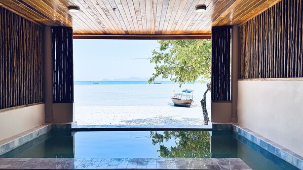 Zona de piscina con vista a una playa y barcos.
