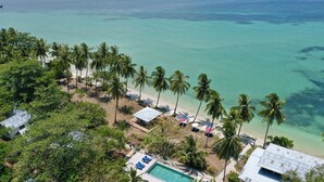 Vista aérea de un complejo turístico con piscina, palmeras y una playa.
