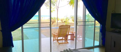 Una habitación con un gran ventanal corredero que da a un patio con una silla y una mesa de madera.