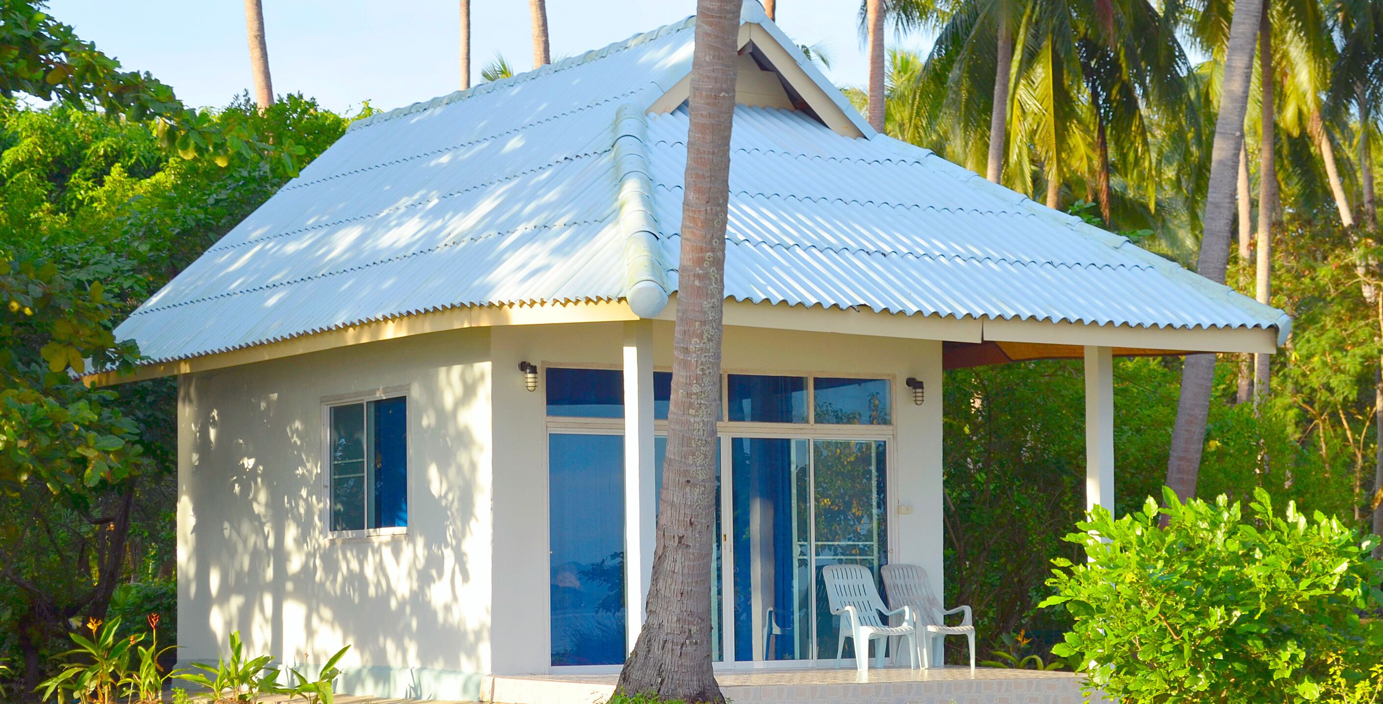 A small, single-story building with a corrugated metal roof, large windows, and a covered porch with two chairs.