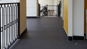Ein Korridor mit einem schwarzen Metallgeländer, weißen Wänden und einer gelben Säule.