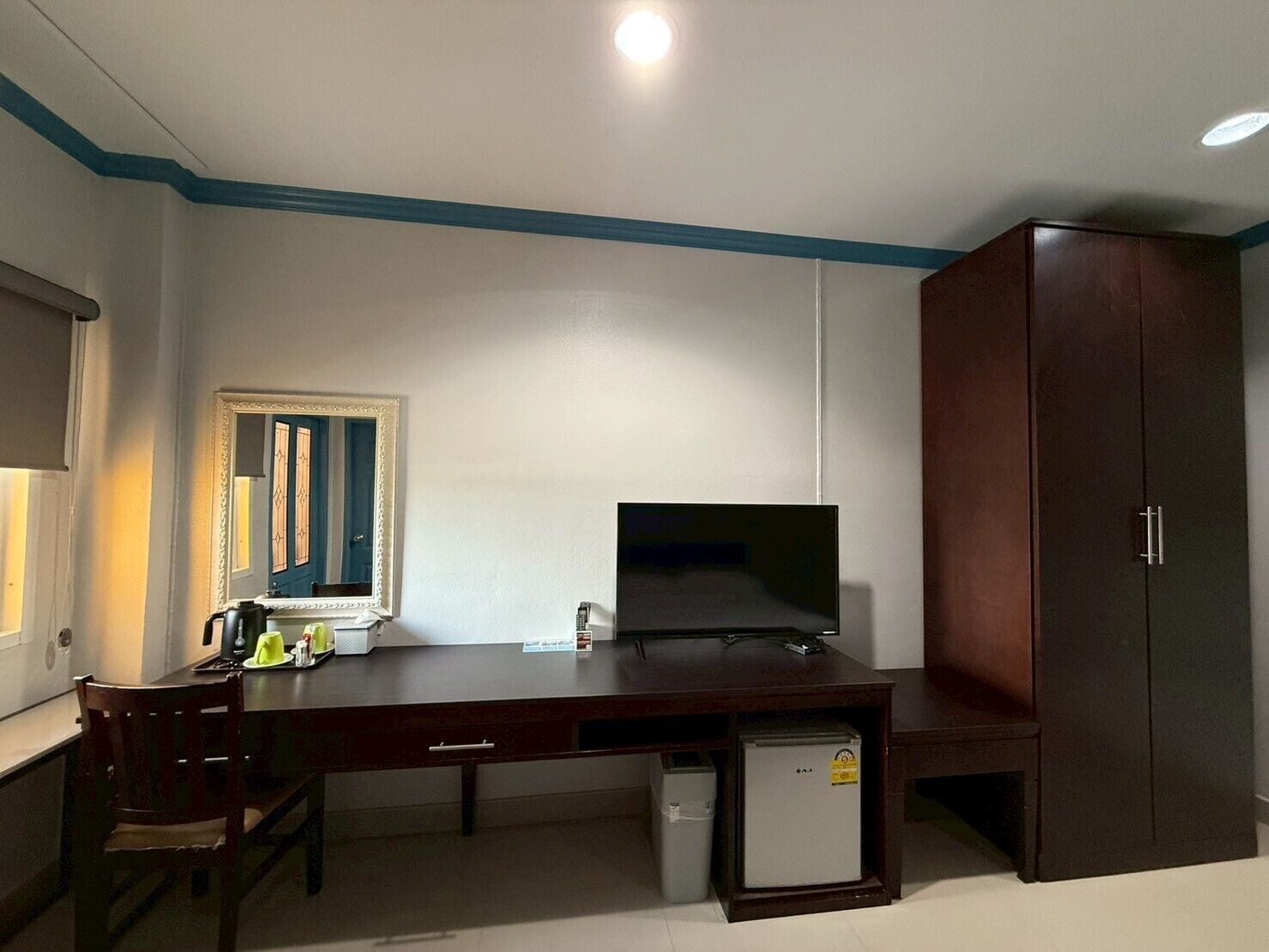 A room with a dark wooden desk, a small refrigerator, a mirror, and a wardrobe.