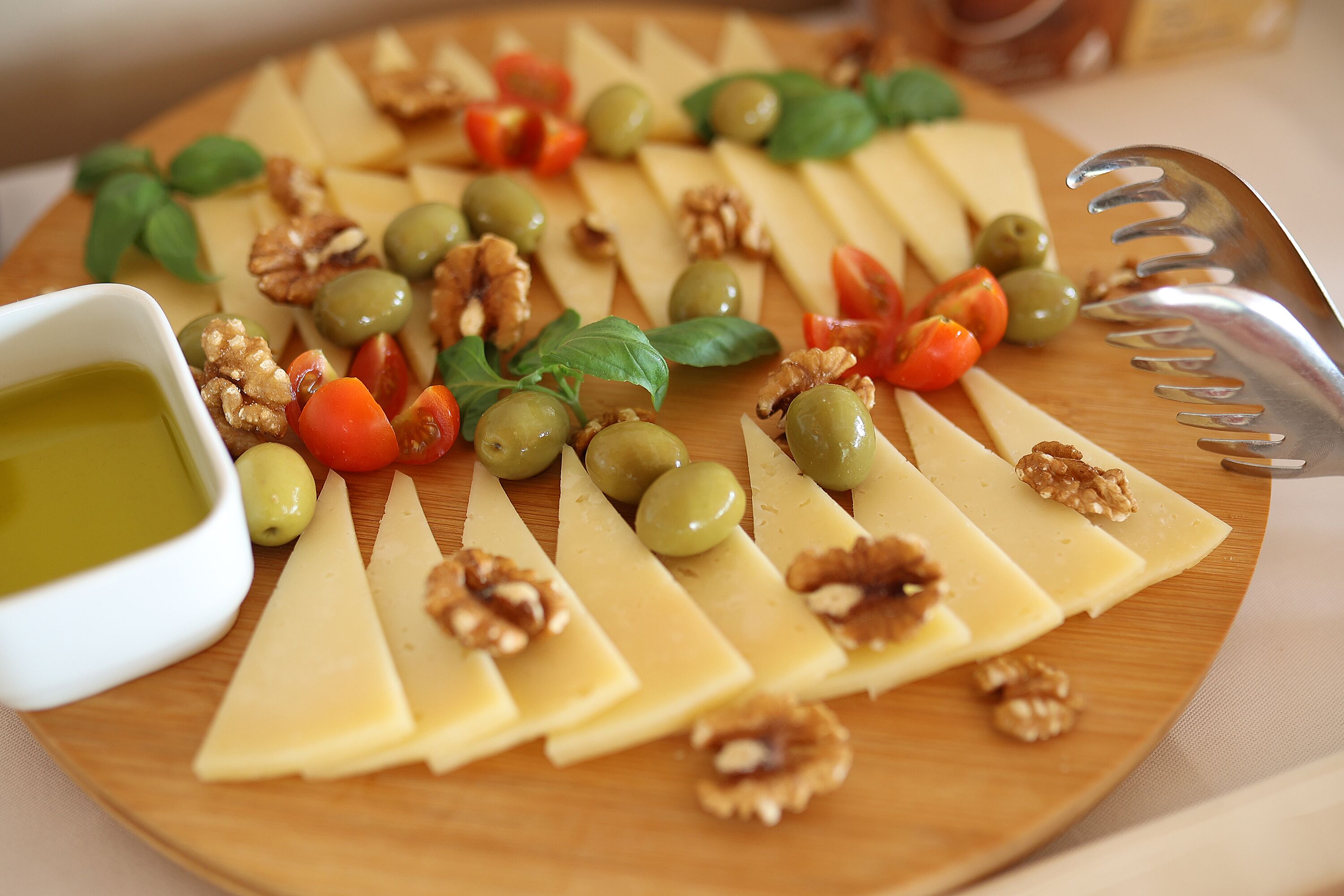 A wooden board with cheese slices, walnuts, olives, and tomatoes.