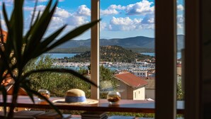 A view from a window overlooking a marina with boats, a town, and mountains in the distance. - Hotel Murter (Murter-Kornati)