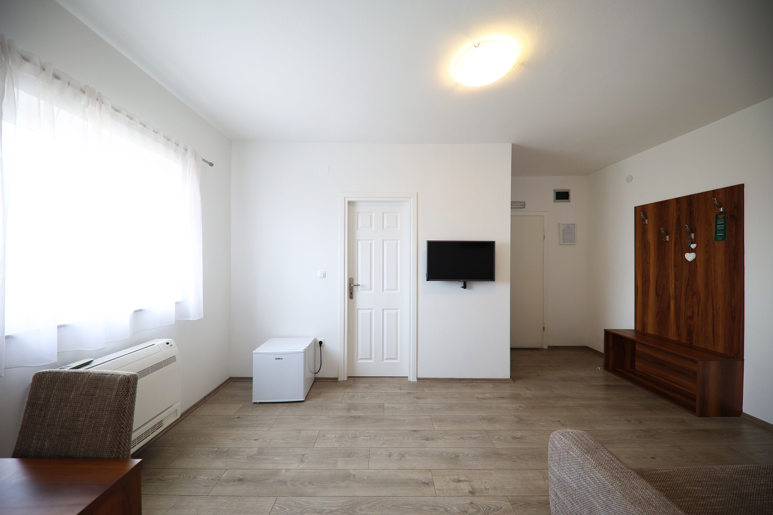 Une pièce avec un plancher en bois, un radiateur blanc, un chauffage d’appoint blanc, un téléviseur fixé au mur et un meuble en bois.