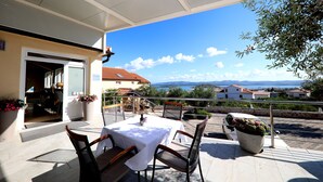 An outdoor patio with a table and chairs, overlooking a scenic view of houses and mountains. - Hotel Murter (Murter-Kornati)