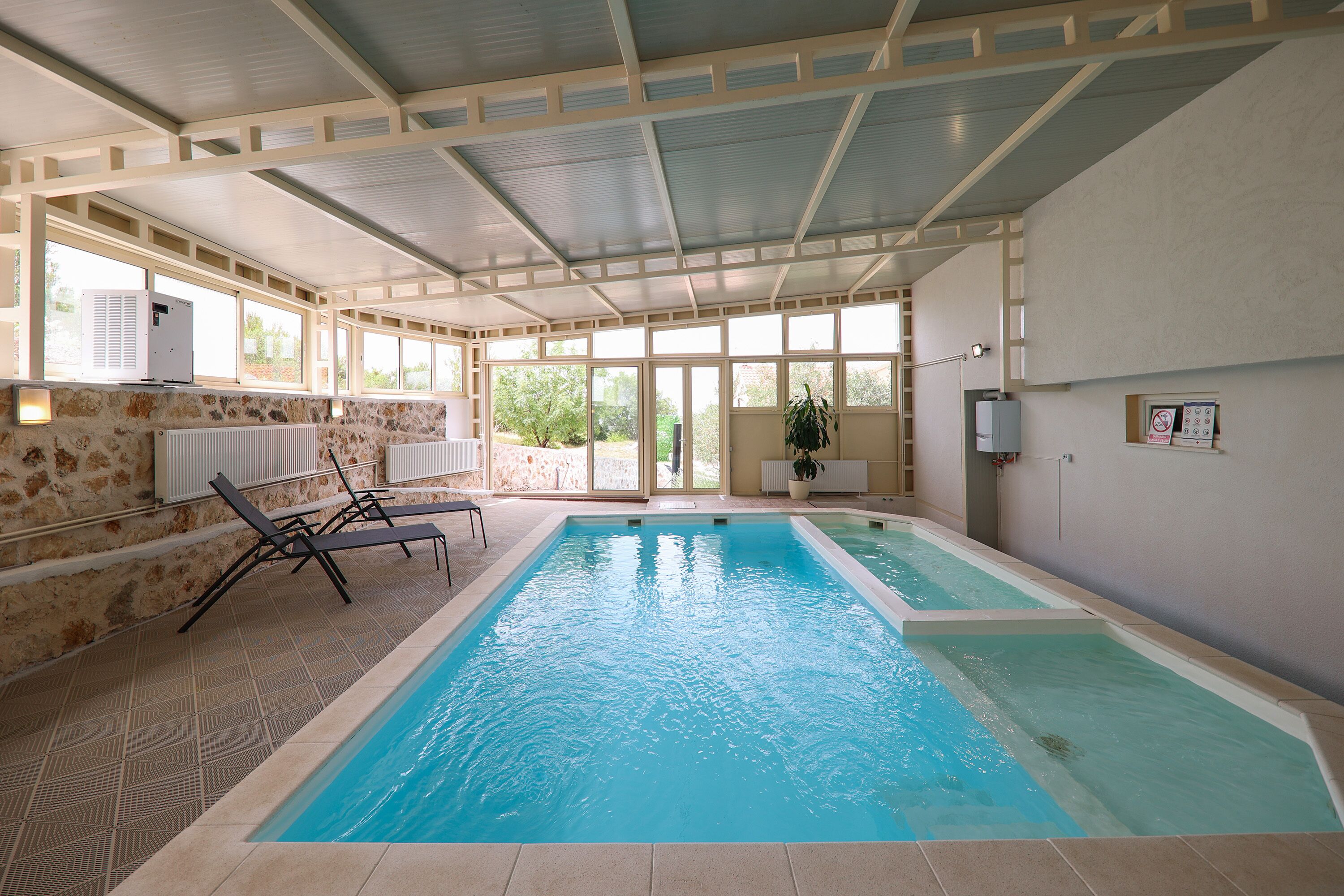 An indoor swimming pool with clear blue water, surrounded by lounge chairs and a stone wall.