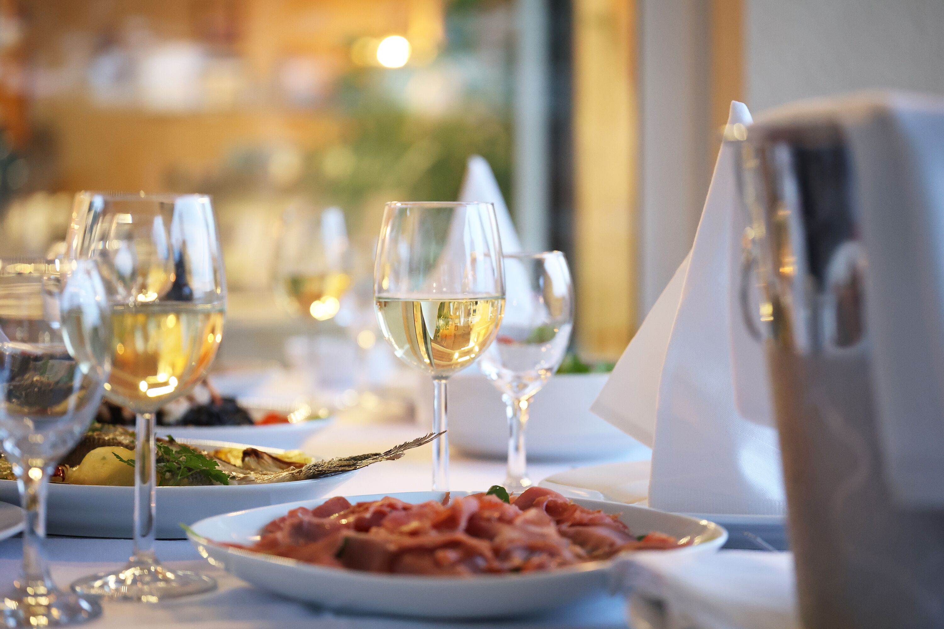 A dining table with multiple wine glasses and plates of food, suggesting a restaurant setting.
