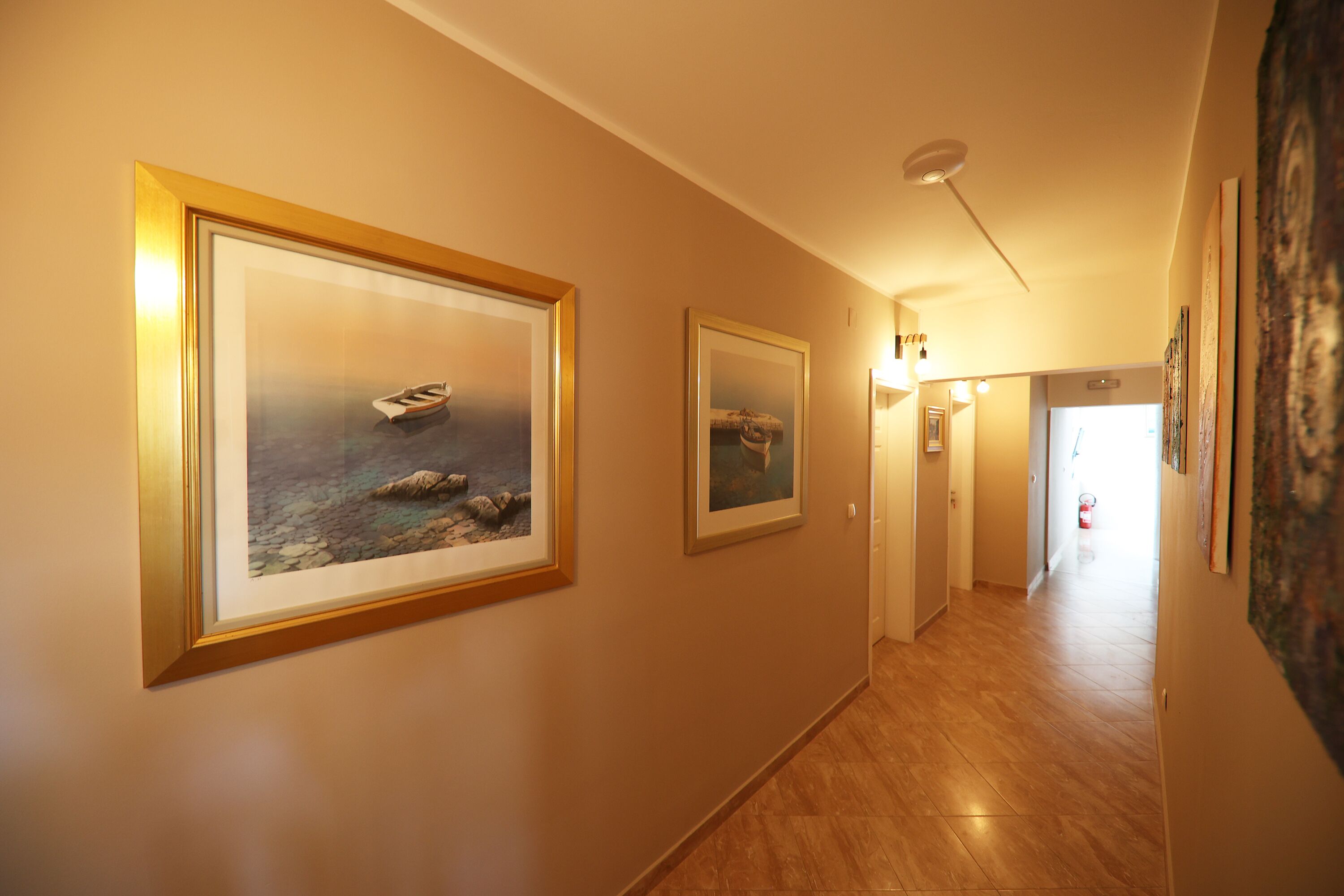 A hallway with framed artwork on the walls, a wooden floor, and a ceiling light.