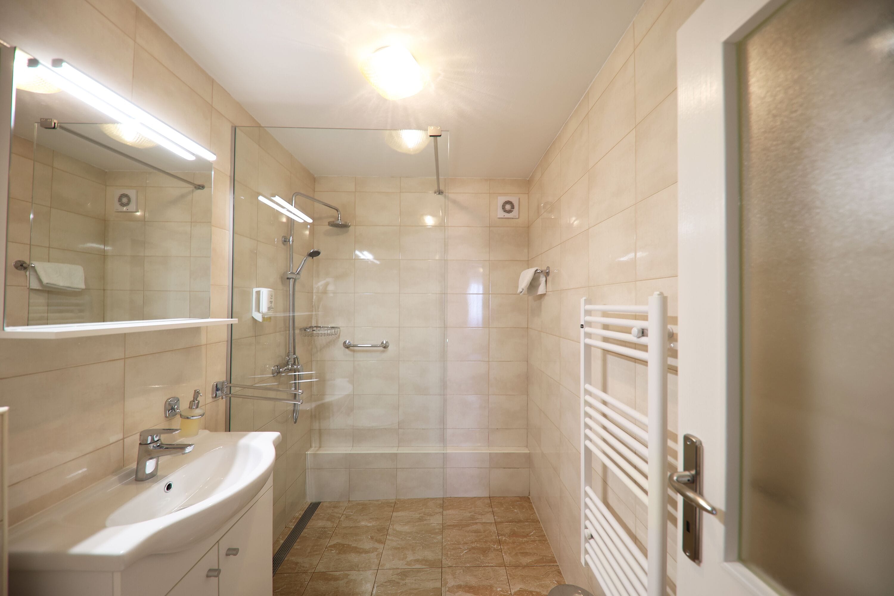 A modern bathroom with a glass shower enclosure, a sink with a soap dispenser, and a towel rack.