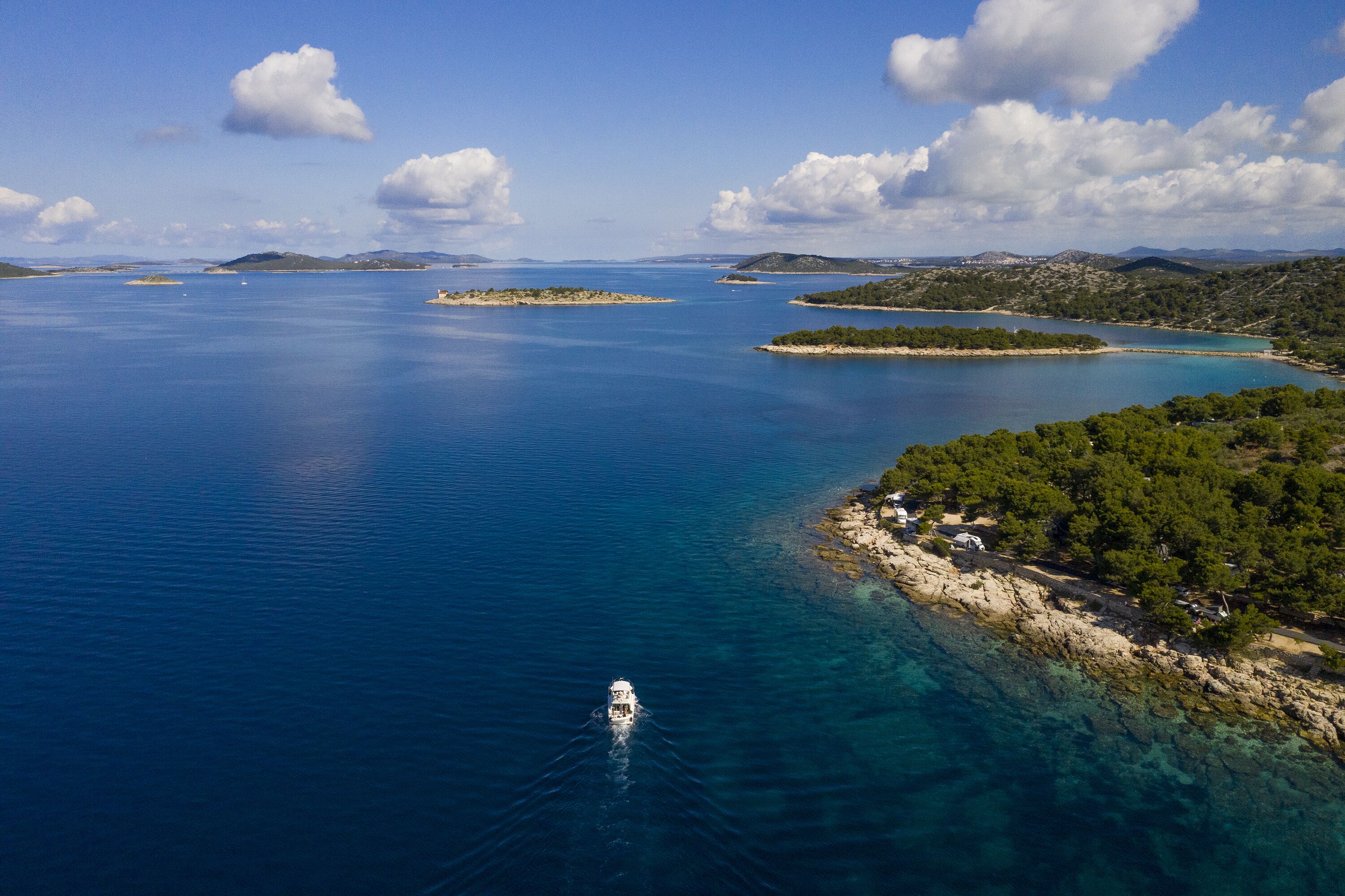 Vista aérea de uma área costeira com águas azul-claras, várias ilhotas e um barco ao longe.