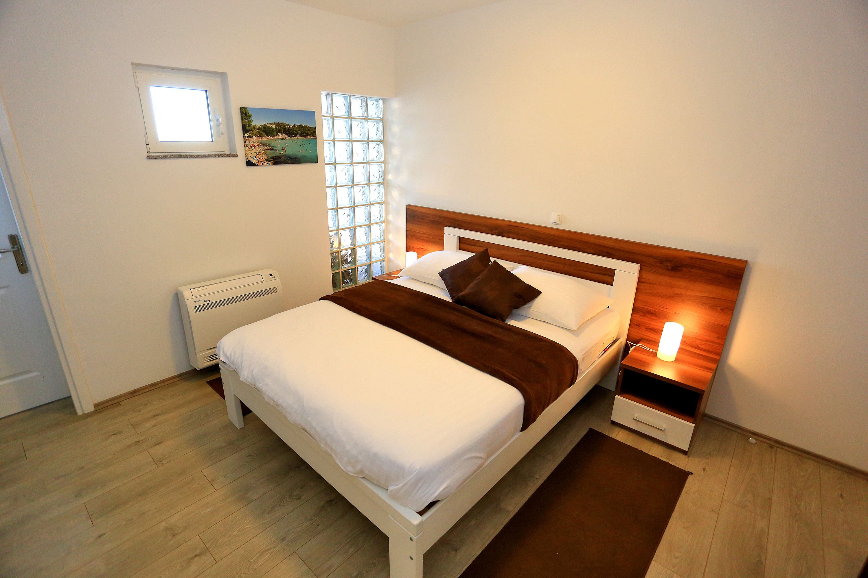 A bedroom with a bed, a nightstand, a heater, a window, and a picture on the wall.