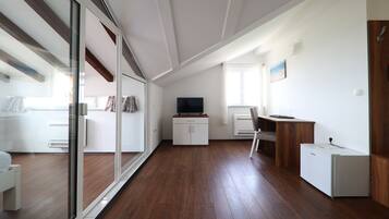 Un apartamento moderno con piso de madera, un televisor de pantalla plana sobre un mueble de madera, un escritorio blanco y un refrigerador compacto.