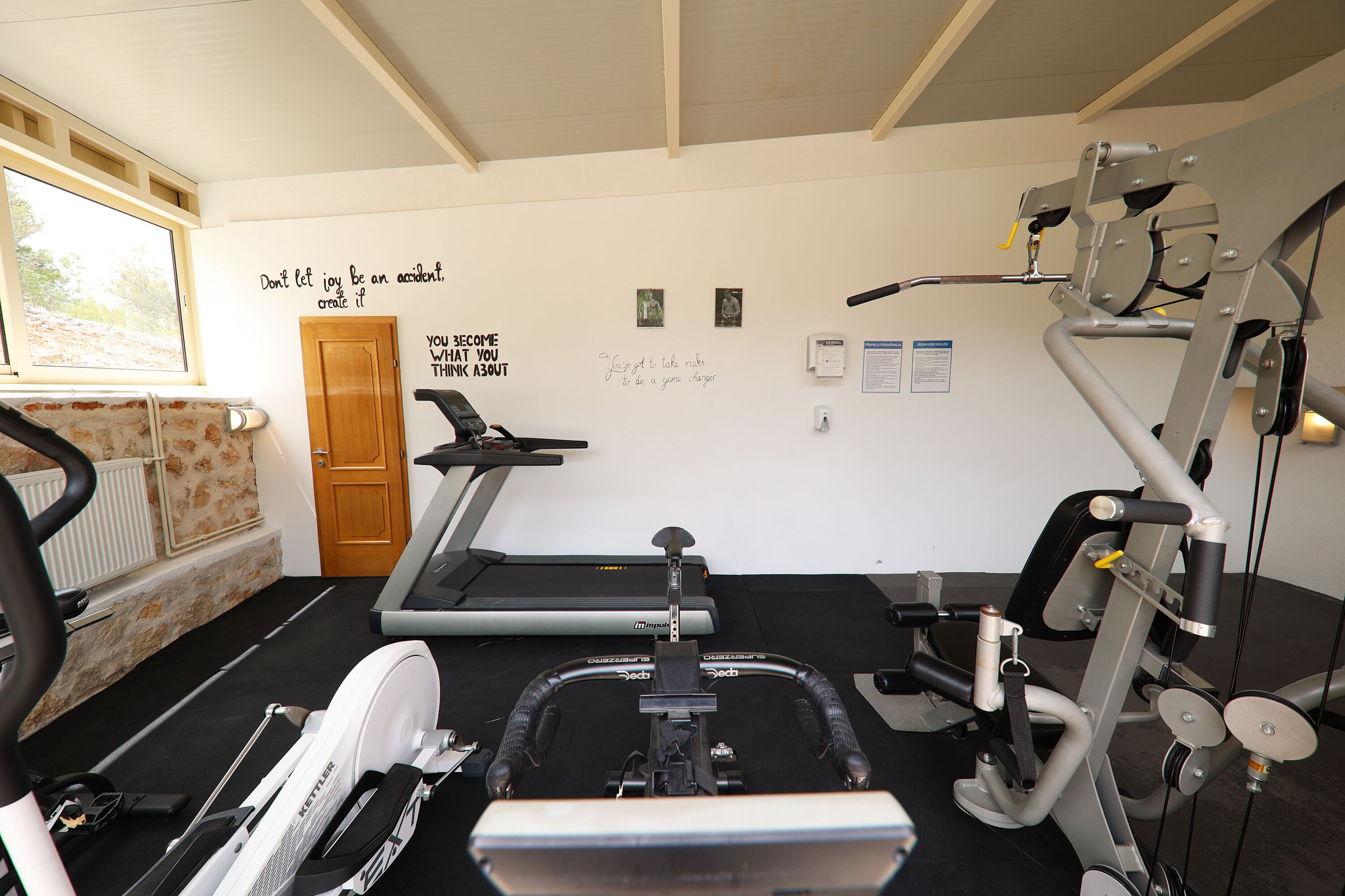 A gym with exercise equipment, motivational wall quotes, and a window with a view of the outdoors.