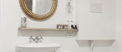 Une salle de bain avec un lavabo blanc, un miroir encadré d’or, des toilettes et une petite étagère contenant des articles de toilette.