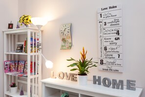 A room with a white shelf displaying magazines, a potted plant, and a wall with 'LOVE' and 'HOME' letters. A wall clock and a sign with 'Love Rules' are also visible. - B&B Vatican's Keys (Rome)