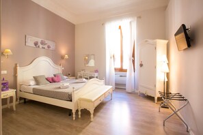 Een slaapkamer met een bed, nachtkastje, lamp en een kapstok.