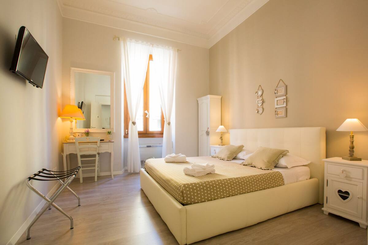 Une chambre à coucher comprenant un lit, une table de chevet, une lampe, un bureau, une chaise et un téléviseur fixé au mur.