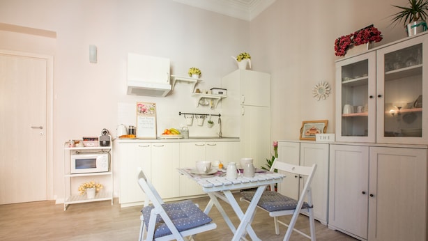 A compact kitchen with white cabinetry, a dining table with chairs, and a small refrigerator. - B&B Vatican's Keys (Rome)