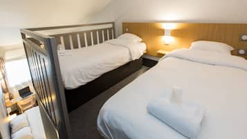 Habitación de hotel con dos camas, un escritorio con una computadora portátil y una mesita de noche con una lámpara.